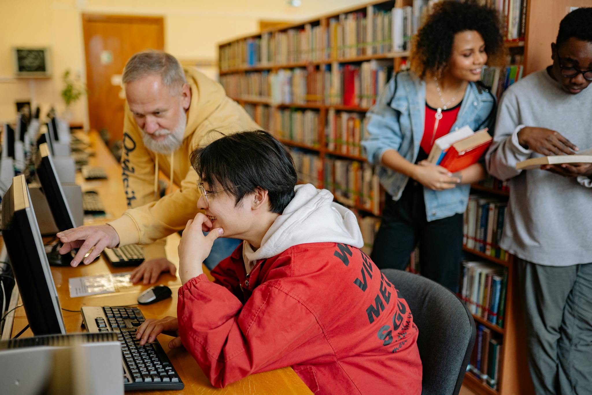 Students collaborating and learning in a library setting, engaging with computers and books.